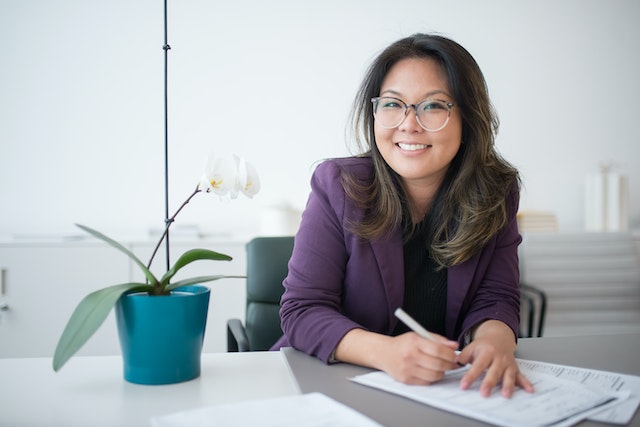 person sitting at their desk smiling with a small plant next to them